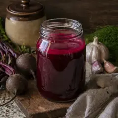 Słoik z kiszonym barszczem czerwonym, obok buraki, czosnek i koperek. Kiszony barszcz czerwony na co pomaga? Na odporność i trawienie!