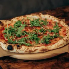 Pyszna pizza z rukolą i szynką, dzieło prawdziwego pizzaiolo, na drewnianym stole.