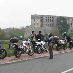 Motocykliści i ich maszyny na tle ruin zamku w pochmurny dzień.
