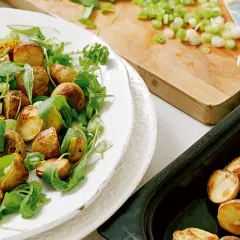 En härlig rostad potatissallad med ruccola och salladslök, redo att serveras.
