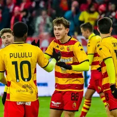 Piłkarze Jagiellonii Białystok świętują. Na boisku w meczu przeciwko Górnikowi Zabrze, zawodnicy w żółto-czerwonych strojach cieszą się z sukcesu.