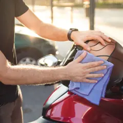 Uomo pulisce il casco da moto con un panno viola. Ricorda, il casco non deve essere pulito con solventi.