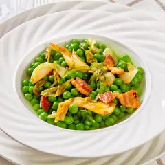 Un plat de petit pois à la française, garni de lardons croustillants et de légumes tendres, servi dans une assiette blanche élégante.