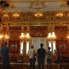 Zachwycająca bursztynowa komnata, gdzie złote zdobienia i światło tworzą magiczną atmosferę. Zwiedzający podziwiają jej piękno.