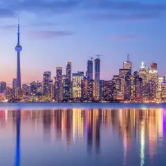 Toronto Skyline bei Dämmerung, ein Muss für jeden Besucher. Der CN Tower ragt empor, beleuchtete Wolkenkratzer spiegeln sich im Wasser.