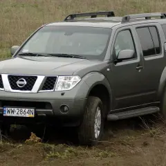 Szary Nissan Pathfinder r51 pokonuje błotniste wzniesienie, wzbijając tumany kurzu.