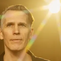 En man med grått hår och blå ögon, badande i solljus. Kanske en artist på en tingsek konsert.