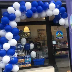 Biało-niebieskie balony tworzą łuk nad wejściem do sklepu z logo Łowicz.