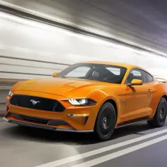 Un Mustang naranja acelera en un túnel, sus potentes sonidos de coches deportivos resonando.