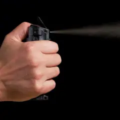 Main d'une personne actionnant une bombe lacrymogène, le jet de gaz se dispersant dans l'air. La loi encadre l'usage de ce type de défense.