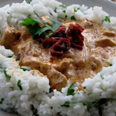 Pyszny kurczak z mascarpone i suszonymi pomidorami, podany z ryżem i posypany natką pietruszki.