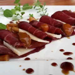 Cienkie plastry bresaoli, ser, marynowane grzyby i sos balsamiczny na białym talerzu. Tak wygląda bresaola, co to za przysmak!