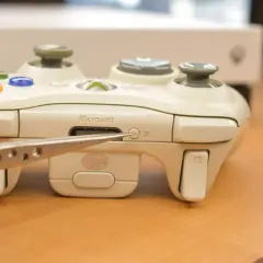 Pęseta zbliża się do przycisku synchronizacji na białym padzie Xbox. Dowiedz się, jak podłączyć drugiego pada Xbox.
