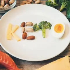 Litery KETO ułożone z sera, orzechów, brokuła i jajka. Czy dieta keto jest zdrowa? Obok łosoś, awokado, oliwa.