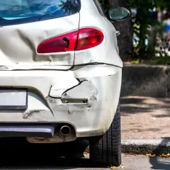 Uszkodzony tył białego samochodu, ślady po kolizji. Kierowca mógł dokonać ucieczka z miejsca kolizji.