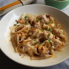 Pyszne ciasto wonton w pikantnym sosie, posypane szczypiorkiem i sezamem. Obok pałeczki w etui.