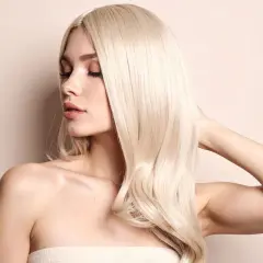 Kobieta z burzą włosów w odcieniu platynowy blond, z zamkniętymi oczami i delikatnym uśmiechem.
