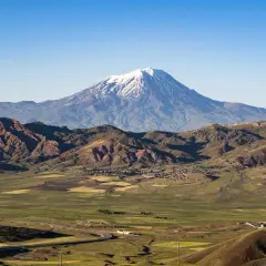 Majestatyczny masyw wulkaniczny w Turcji, Ararat, góruje nad zieloną doliną z polami uprawnymi i krętą drogą.