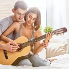 Para tworzy najpiękniejsze melodie o miłości, grając razem na gitarze w przytulnym pokoju.
