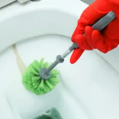 Mano con guanto rosso pulisce il WC con uno scopino verde per togliere il calcare.
