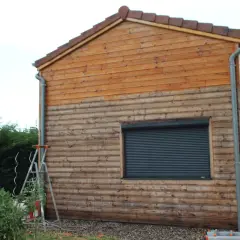 Échelle près d'un mur en bois, suggérant un entretien du bardage bois. Le bois est plus clair en haut, plus foncé en bas.