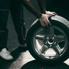 Mechanik w rękawiczkach trzyma koło z felgą, gotowy do wymiany przebitej opony.