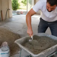 Un ouvrier prépare le mélange pour le dosage chape pour carrelage, mélangeant ciment et sable dans une brouette.