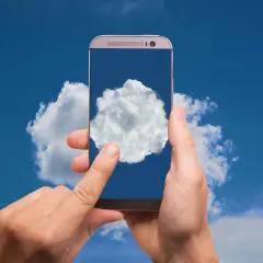 Dłonie trzymają telefon, na którego ekranie widać chmurę. To symbol tego, gdzie jest chmura w telefonie – w chmurze danych.