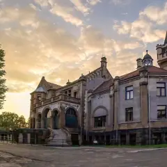 Pałac Schönów w Sosnowcu, co zobaczyć? Imponująca budowla z wieżyczkami i łukami, otoczona zielenią, przy zachodzącym słońcu.