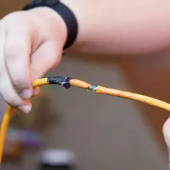 Dłonie łączące pomarańczowy kabel, pokazując jak połączyć kable bez lutowania za pomocą taśmy izolacyjnej.