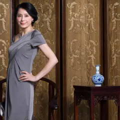 Elegancka mama pana młodego w szarej sukience, z dłonią na biodrze, pozuje na tle zdobionych paneli.