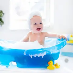 Radosny noworodek w pianie podczas kąpieli w niebieskiej wanience z gumowymi kaczuszkami.