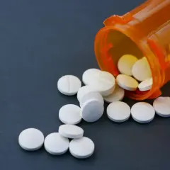 Białe tabletki rozsypane z pomarańczowego pojemnika. Niektóre z nich mogą zawierać fentanyl, substancję o silnym działaniu.