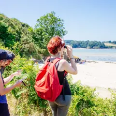 Couple en randonnée à Saint-Jacut-de-la-Mer, consultant une carte. Une femme observe la baie avec des jumelles.