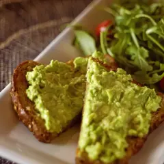 Dwie kromki pełnoziarnistego chleba z najpyszniejszym guacamole, obok sałatka z rukoli i pomidorki koktajlowe.