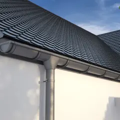 Szare elementy rynny odprowadzają wodę z ciemnego, łupkowego dachu.