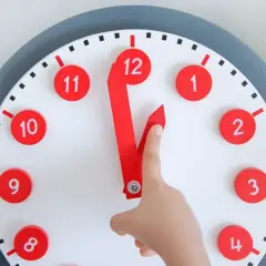 Un niño aprende las horas con un reloj didáctico. Las manecillas rojas apuntan a las 12 y las 11.