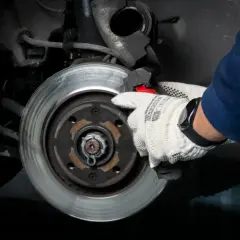 Ręka w rękawicy wymienia klocki hamulcowe, by uniknąć metaliczny pisk podczas jazdy.