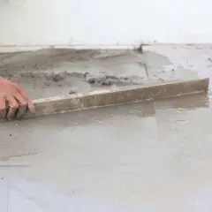 Ręka pracownika wyrównuje świeżą wylewkę betonową. Zastanawiasz się, ile waży wylewka betonowa?