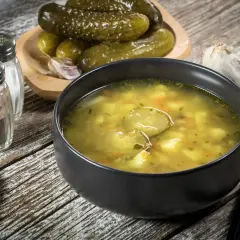 Miseczka zupy ogórkowej, obok miseczka z ogórkami kiszonymi i przyprawy. Czy zupę ogórkową się zagęszcza?