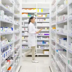 Farmaceutka w białym fartuchu przeszukuje półki apteki, szukając leku milurit 300.