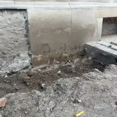Prace przy fundamencie: odsłonięta ściana, ziemia i gruz. Widać fragmenty cegieł i beton. To etap prac, jak podlać fundamenty.