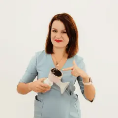 Kobieta w niebieskim uniformie wskazuje na nowoczesny laktator. To urządzenie, które może ułatwić życie mamom, jak i pomóc w pielęgnacji skóry, np. przy problemach z cerą, gdzie milanella complex jest często polecany.