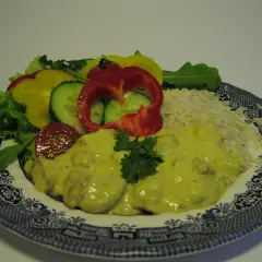 En tallrik med kyckling curry, ris och en sallad av paprika, gurka och tomat.
