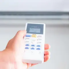 Mano ajustando el control remoto del aire acondicionado a 25 grados para una temperatura ideal de calefacción o refrigeración.