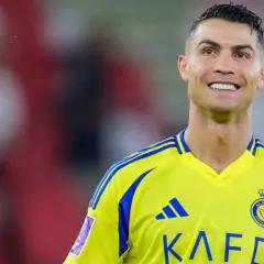 Uśmiechnięty Cristiano Ronaldo w żółtej koszulce z niebieskimi pasami, grający w klubie Al Nassr.