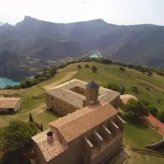 Edificio histórico en la Serra de Busa, con un lago turquesa y montañas al fondo.