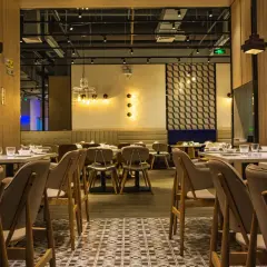 Przytulne wnętrze restauracji z drewnianymi panelami i stylowym oświetleniem. Stoliki nakryte, gotowe na gości.