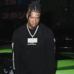 Raper z tatuażami na twarzy, znany jako blueface, pozuje obok jaskrawozielonego samochodu sportowego.