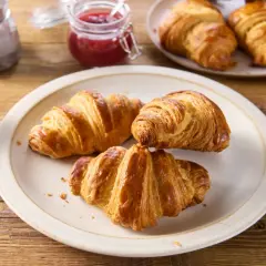 Talerz z trzema złotymi croissantami, filiżanka kawy, słoiczek dżemu i kawiarka.